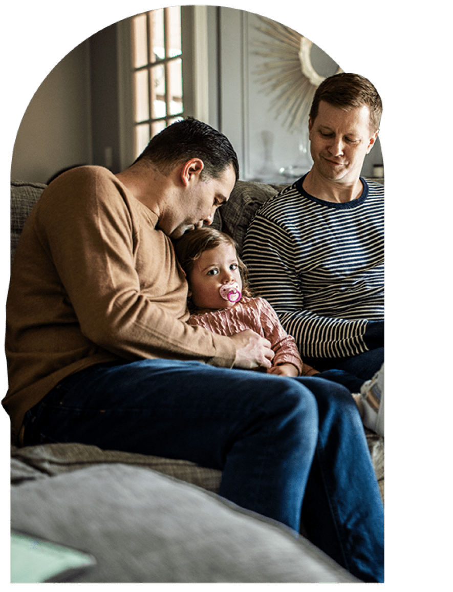 Two men sitting on couch at home caring for a small child sitting between them