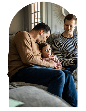Two men sitting on couch at home caring for a small child sitting between them