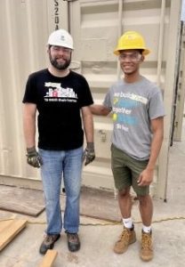 Two people smile at the camera wearing hard hats.